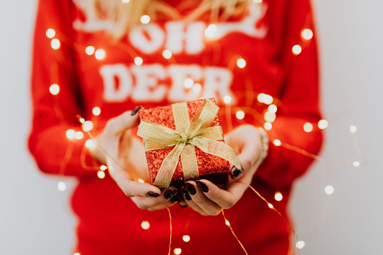 Žena u crvenom džemperu drži novogodišnji paketić.
