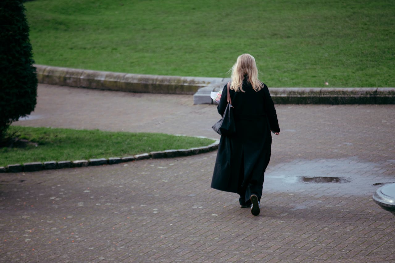 Žena plave kose, slikana otpozadi šeta parkom