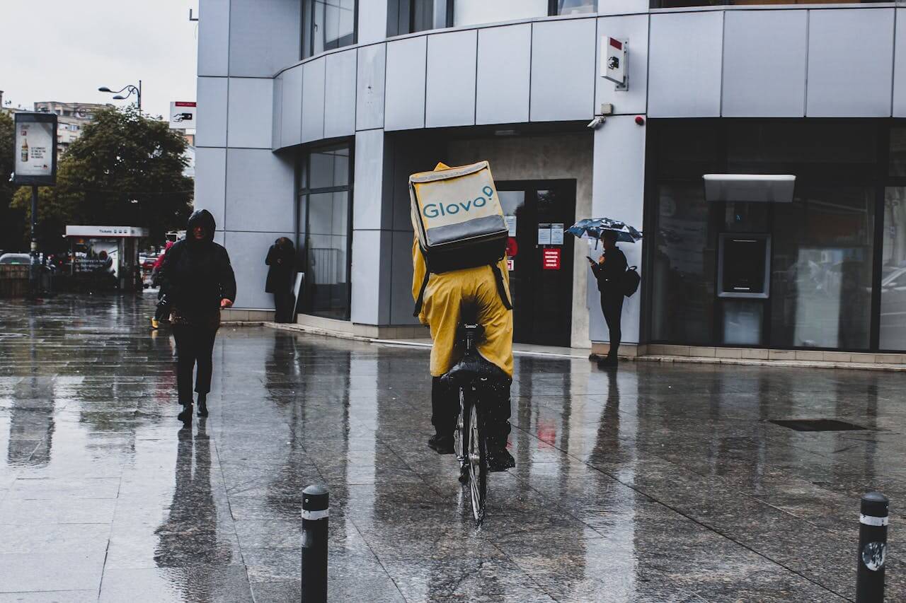 Dostavljač hrane, u žutom odelu, sa torbom Glovo, na bicikli