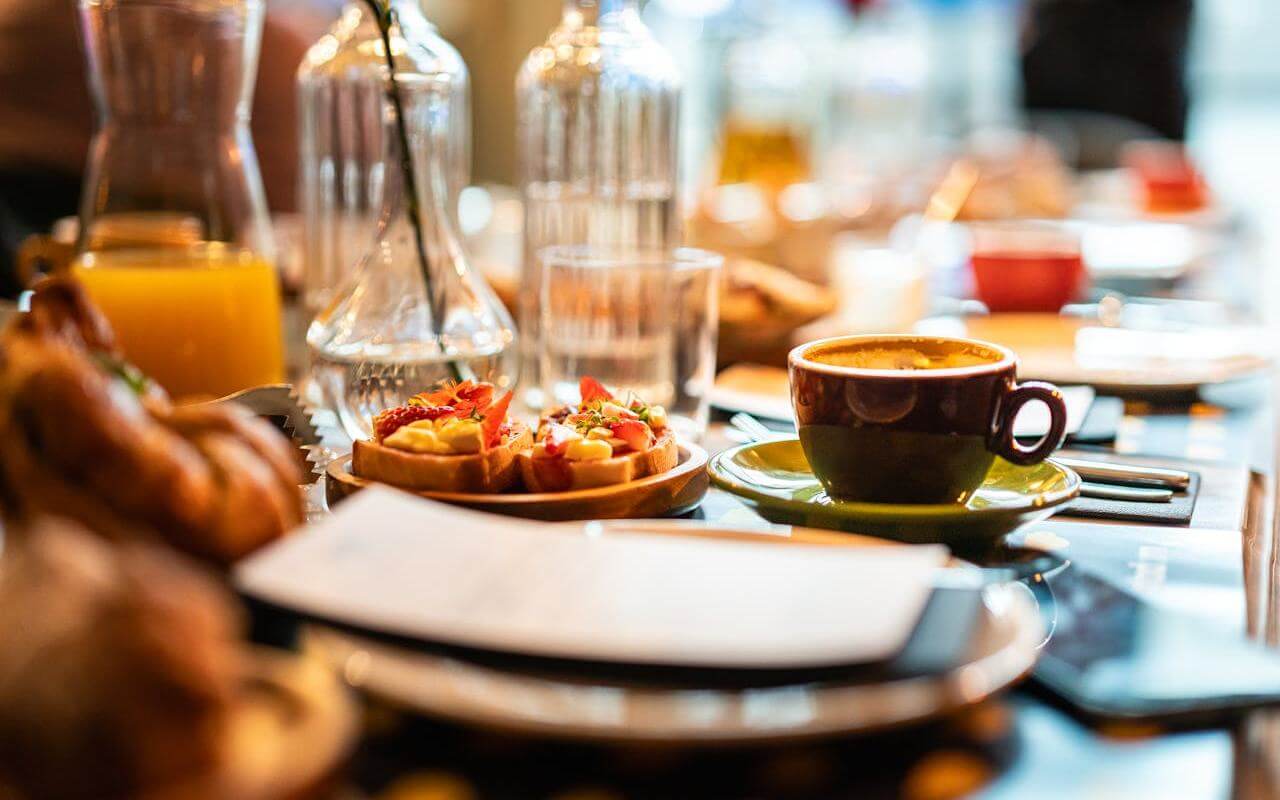 Šoljica espreso kafe, voćni vafli i svež sok na stolu postavljenom za doručak