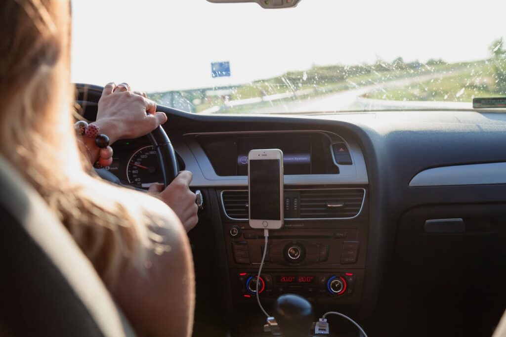 Vozač drži volan, dok je mobilni telefon postavljen na nosač u unutrašnjosti automobila.