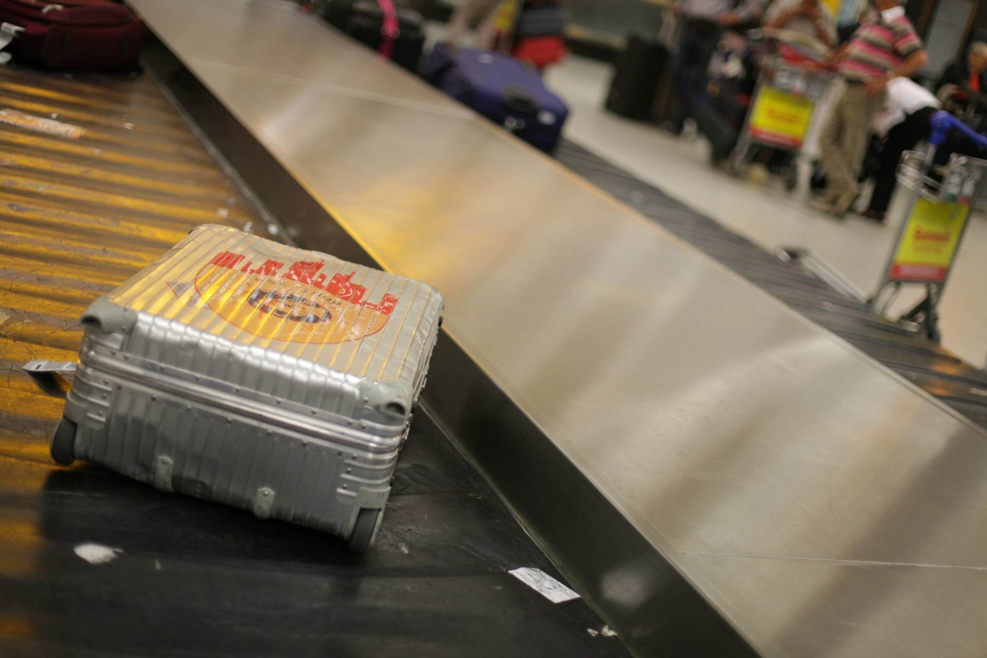 Srebrni kofer sa nalepnicama na traci na aerodromu. 